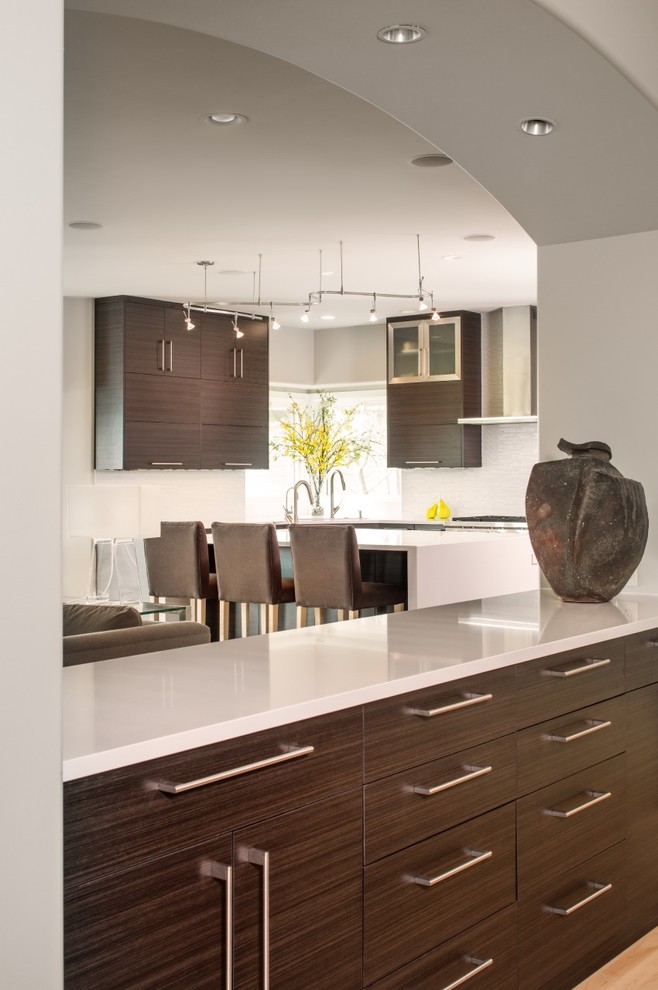 Mid-sized transitional u-shaped light wood floor eat-in kitchen photo in Omaha with an island, an undermount sink, flat-panel cabinets, brown cabinets, quartz countertops, white backsplash, glass sheet backsplash and paneled appliances