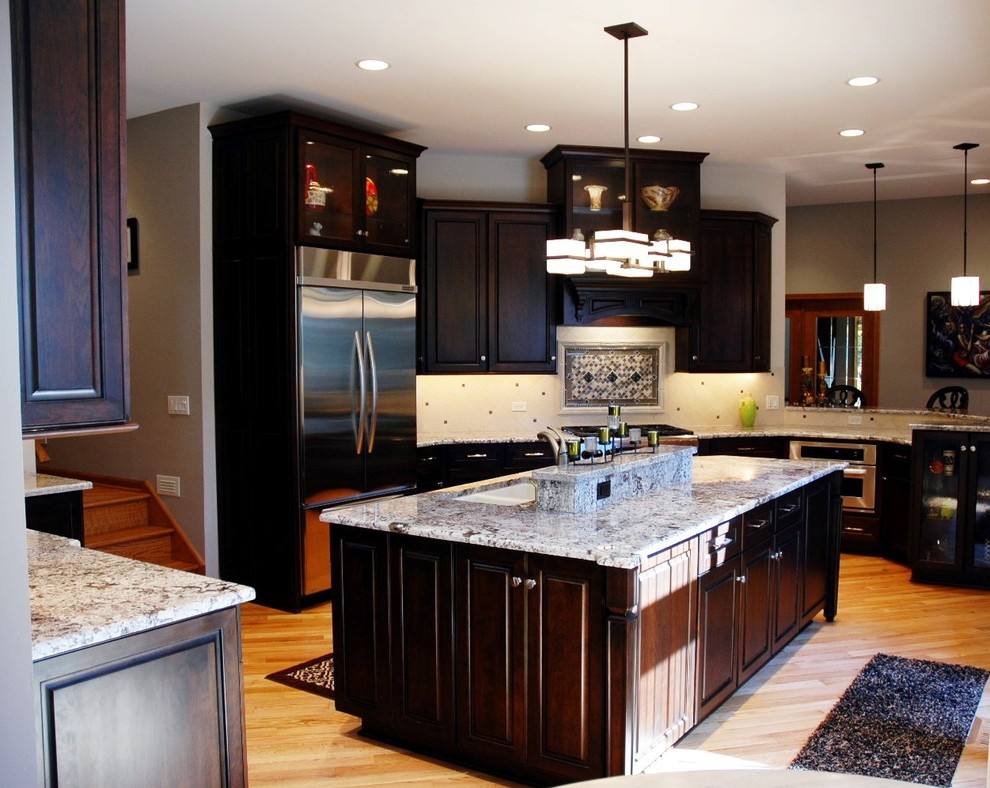 Inspiration for a transitional u-shaped eat-in kitchen remodel in Chicago with an undermount sink, raised-panel cabinets, dark wood cabinets, granite countertops, white backsplash, porcelain backsplash and stainless steel appliances