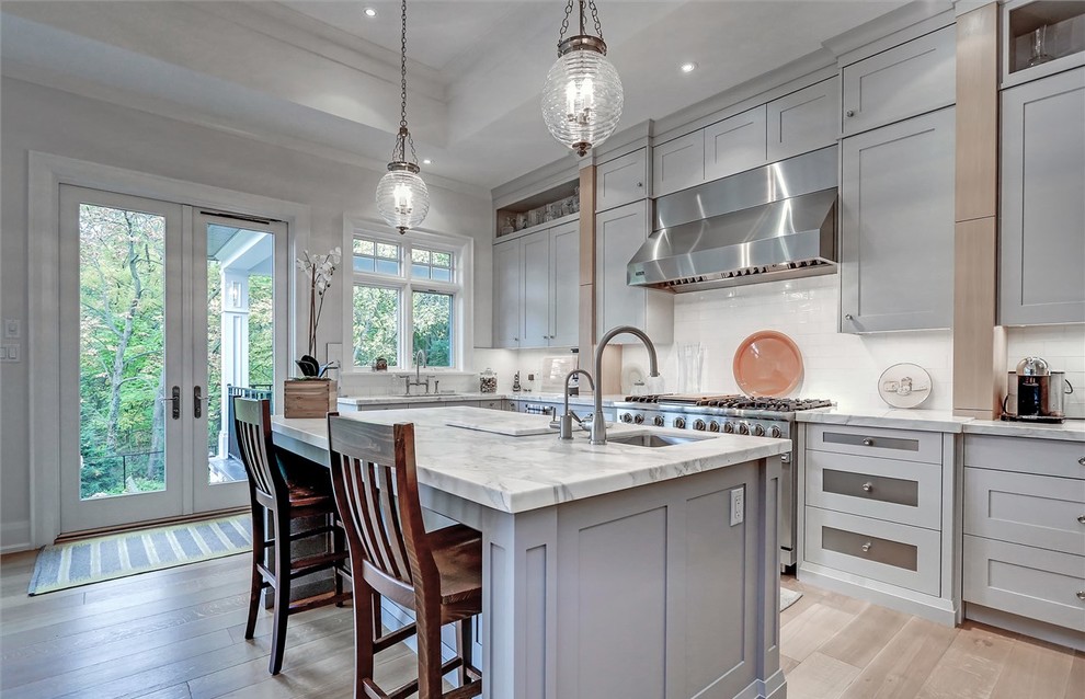 Inspiration for a traditional galley kitchen in Toronto with a submerged sink, shaker cabinets, grey cabinets, white splashback, stainless steel appliances, medium hardwood flooring and an island.