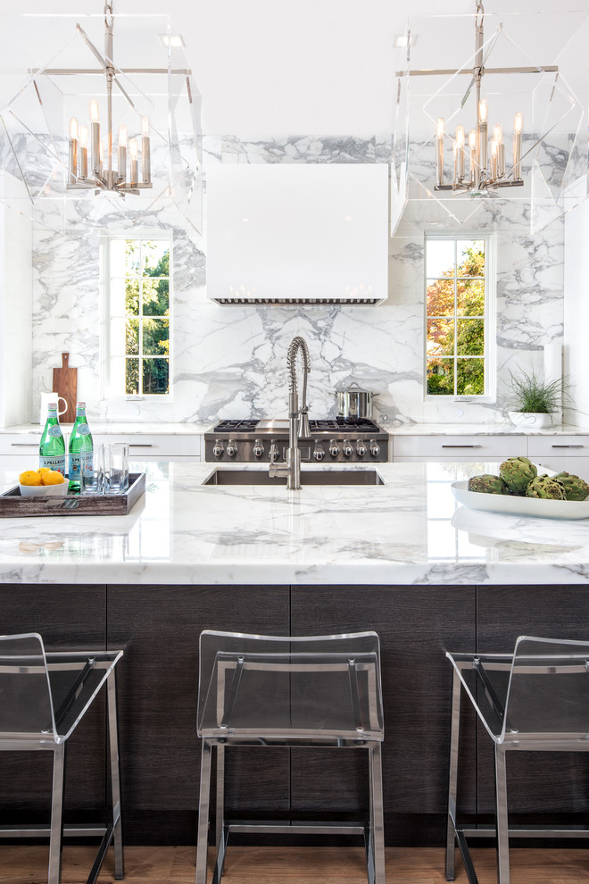Klassisk inredning av ett kök, med en undermonterad diskho, släta luckor, marmorbänkskiva, rostfria vitvaror, en köksö, vita skåp, vitt stänkskydd, stänkskydd i sten och mellanmörkt trägolv