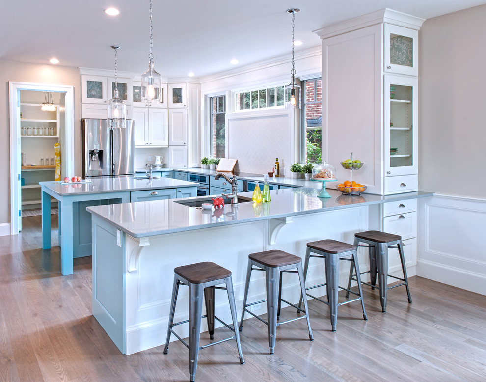 Photo of a large classic u-shaped kitchen/diner in Other with a submerged sink, white cabinets, white splashback, stainless steel appliances, light hardwood flooring, composite countertops, an island and recessed-panel cabinets.