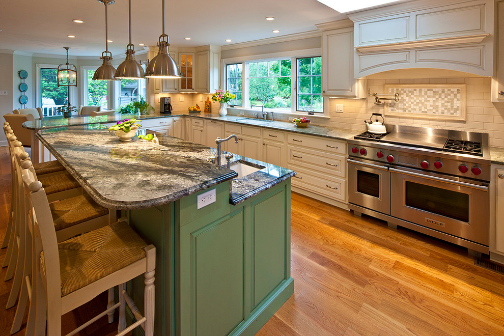 Klassisk inredning av ett kök, med en undermonterad diskho, luckor med upphöjd panel, gröna skåp, granitbänkskiva, beige stänkskydd, stänkskydd i stenkakel, rostfria vitvaror och mellanmörkt trägolv