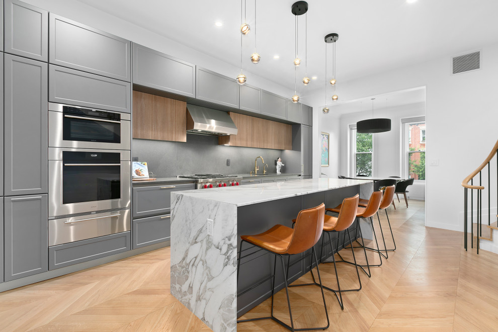 Zweizeilige, Mittelgroße Klassische Wohnküche mit Schrankfronten im Shaker-Stil, grauen Schränken, Kücheninsel, Küchenrückwand in Grau, braunem Holzboden, beigem Boden und grauer Arbeitsplatte in New York