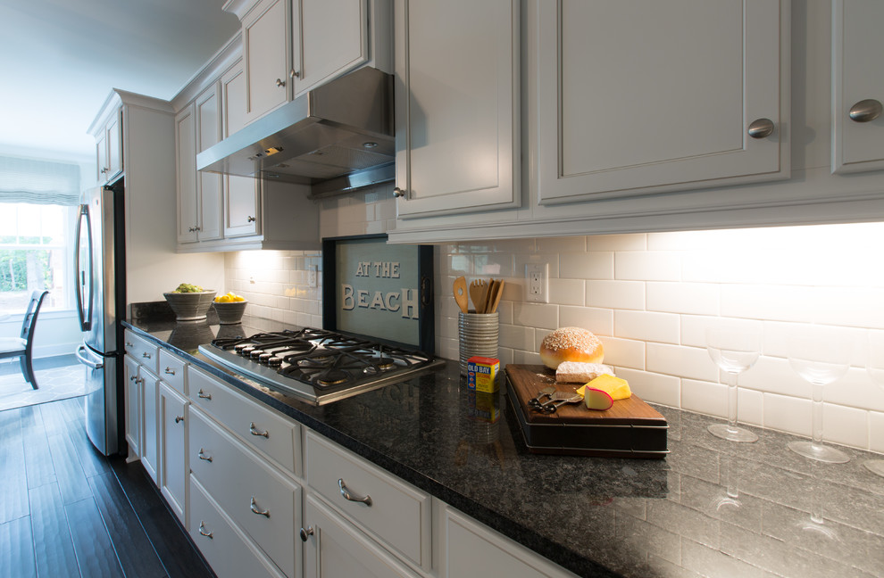 This is an example of a large classic kitchen in DC Metro with a submerged sink, flat-panel cabinets, granite worktops, white splashback, metro tiled splashback, stainless steel appliances, dark hardwood flooring and an island.