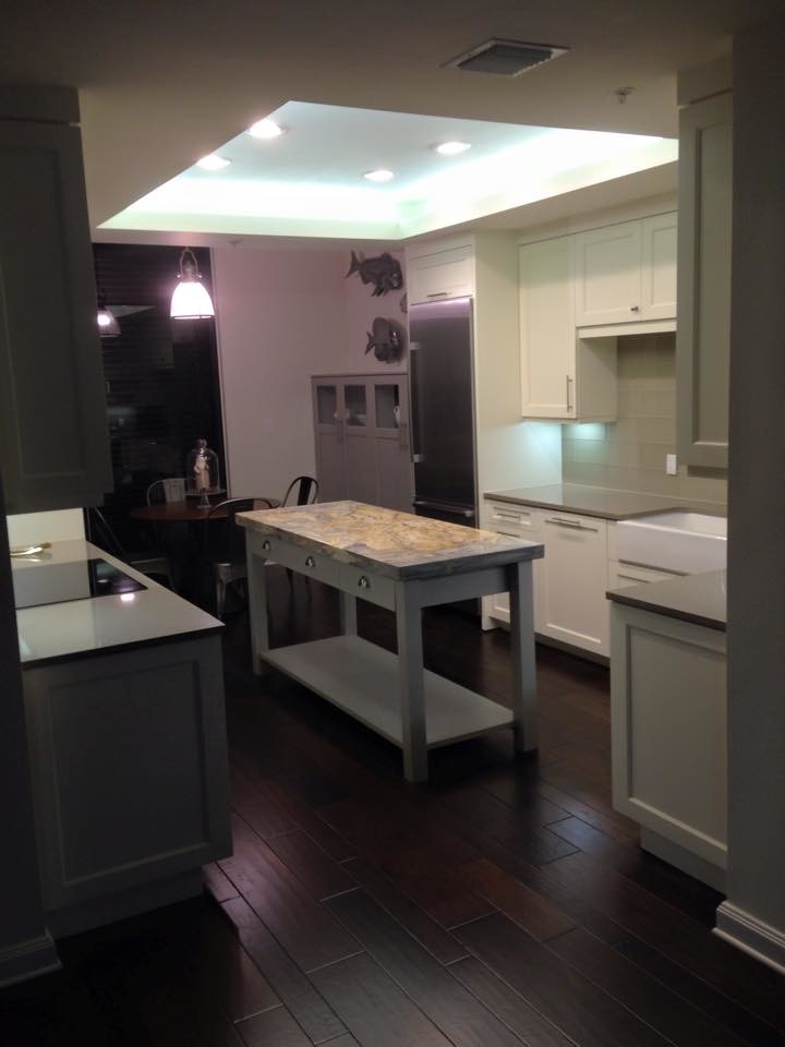 Example of a mid-sized transitional dark wood floor and brown floor enclosed kitchen design in Tampa with a farmhouse sink, shaker cabinets, white cabinets, solid surface countertops, gray backsplash, glass tile backsplash, stainless steel appliances and an island