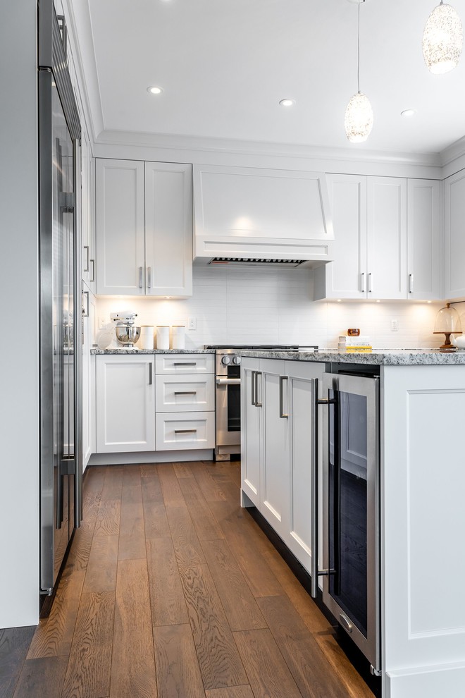 Exempel på ett stort klassiskt flerfärgad flerfärgat kök, med en undermonterad diskho, luckor med infälld panel, vita skåp, granitbänkskiva, vitt stänkskydd, stänkskydd i tunnelbanekakel, rostfria vitvaror, mellanmörkt trägolv, en köksö och brunt golv