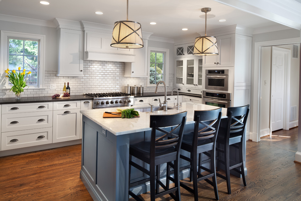 Example of a large transitional u-shaped dark wood floor eat-in kitchen design in Detroit with a drop-in sink, recessed-panel cabinets, white cabinets, white backsplash, ceramic backsplash, stainless steel appliances, an island and marble countertops