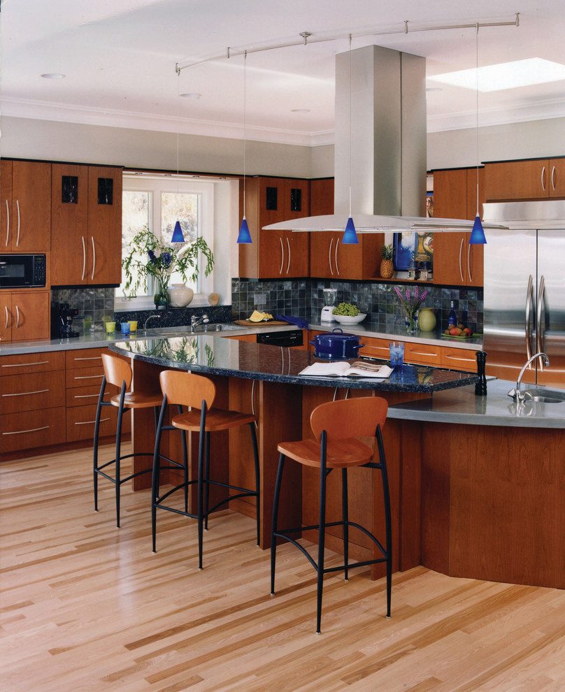 Modern inredning av ett avskilt, mellanstort l-kök, med en integrerad diskho, släta luckor, skåp i mellenmörkt trä, granitbänkskiva, grått stänkskydd, stänkskydd i skiffer, rostfria vitvaror, ljust trägolv, en köksö och beiget golv