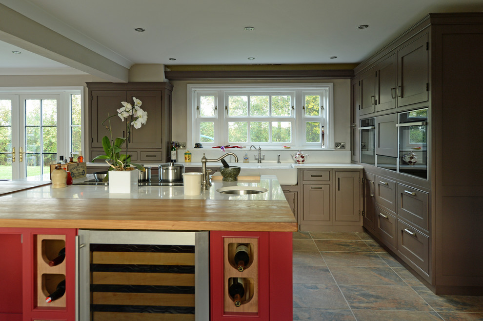 Inredning av ett klassiskt kök och matrum, med en dubbel diskho, luckor med infälld panel, bruna skåp, träbänkskiva, vitt stänkskydd, rostfria vitvaror och en köksö