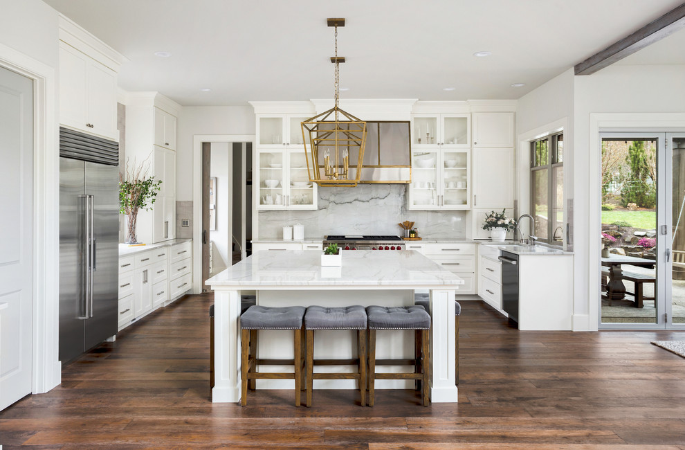 Inspiration for a traditional u-shaped kitchen in San Francisco with a belfast sink, shaker cabinets, white cabinets, white splashback, stone slab splashback, stainless steel appliances, medium hardwood flooring, an island, brown floors and white worktops.