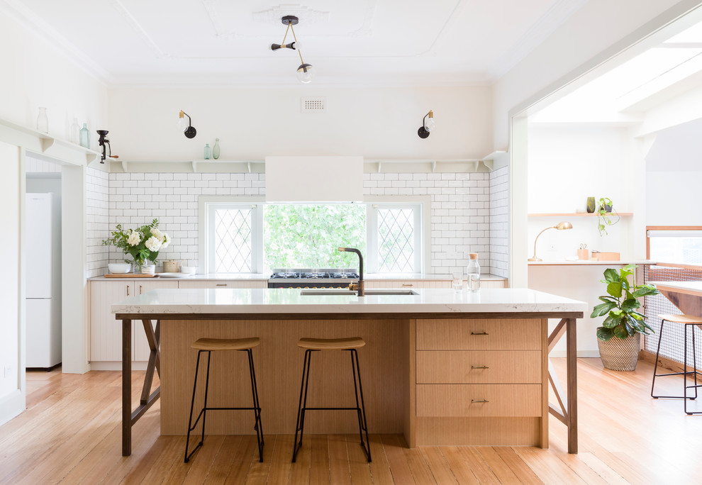 メルボルンにあるトランジショナルスタイルのおしゃれなアイランドキッチン (アンダーカウンターシンク、フラットパネル扉のキャビネット、白いキッチンパネル、サブウェイタイルのキッチンパネル、淡色無垢フローリング) の写真