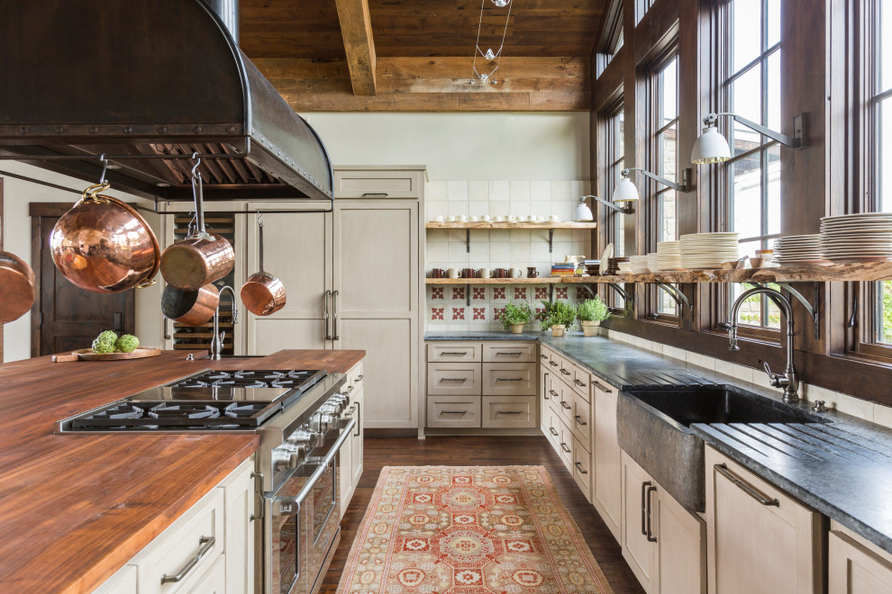 Photo of a large rustic u-shaped kitchen/diner in Houston with a belfast sink, shaker cabinets, beige cabinets, soapstone worktops, white splashback, porcelain splashback, stainless steel appliances, medium hardwood flooring, an island, brown floors, grey worktops and a wood ceiling.