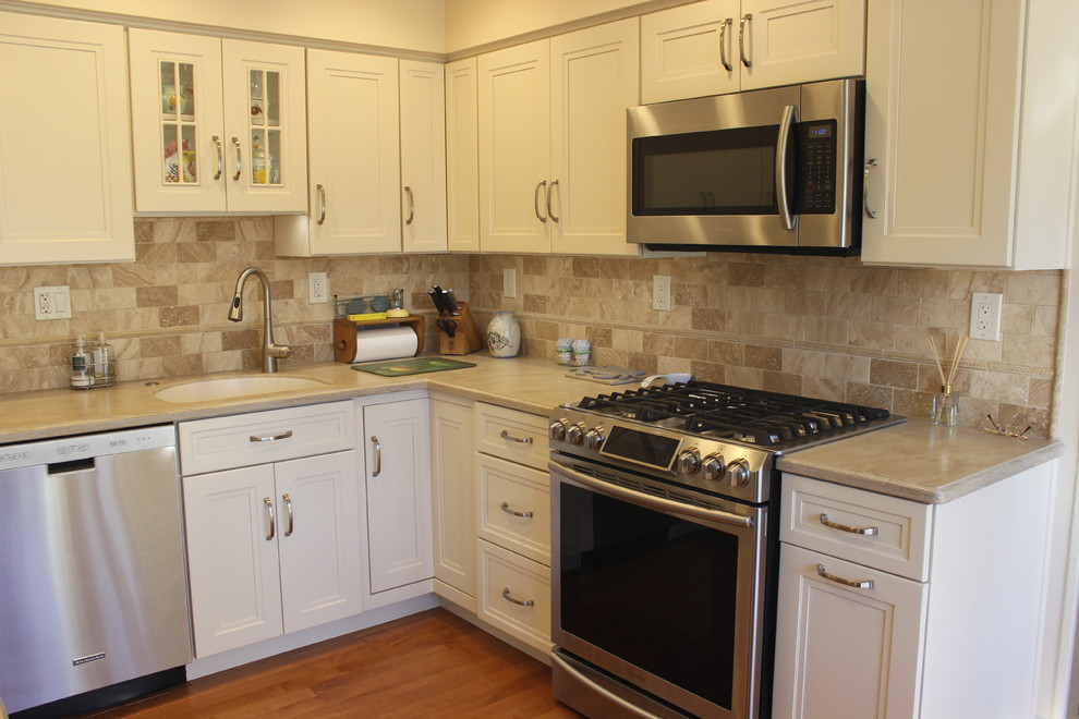 Exempel på ett avskilt, litet klassiskt u-kök, med en undermonterad diskho, luckor med infälld panel, vita skåp, beige stänkskydd, stänkskydd i sten, rostfria vitvaror och ljust trägolv