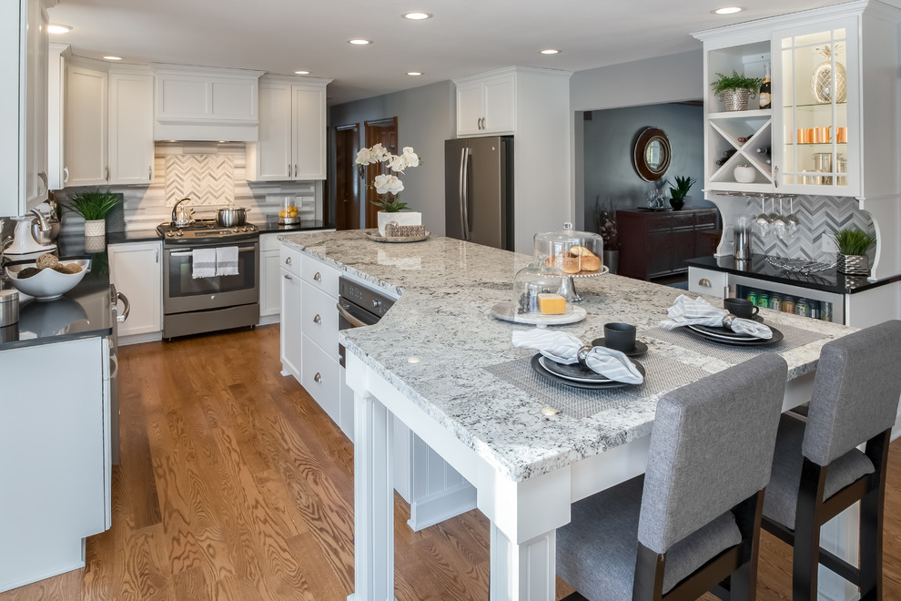 Design ideas for a classic u-shaped kitchen in Milwaukee with white cabinets, granite worktops, grey splashback, marble splashback, stainless steel appliances, medium hardwood flooring, an island, shaker cabinets and brown floors.
