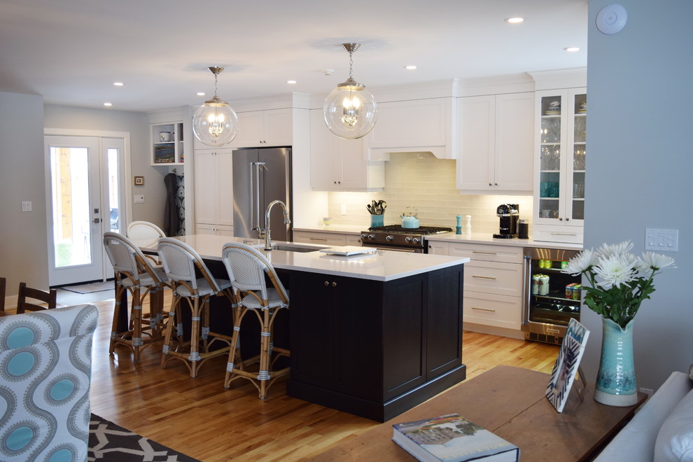 Traditional kitchen/diner in Ottawa with a single-bowl sink, shaker cabinets, white cabinets, engineered stone countertops, beige splashback, glass tiled splashback, stainless steel appliances, light hardwood flooring and an island.