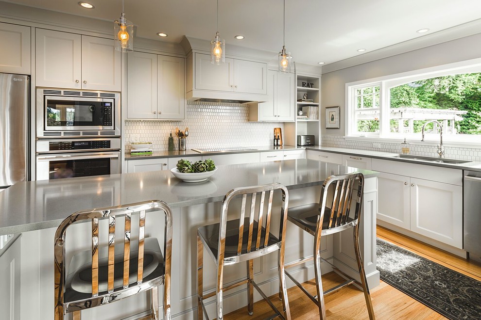 Inspiration for a mid-sized transitional l-shaped medium tone wood floor eat-in kitchen remodel in Vancouver with a double-bowl sink, shaker cabinets, gray cabinets, quartz countertops, white backsplash, stainless steel appliances, an island and ceramic backsplash