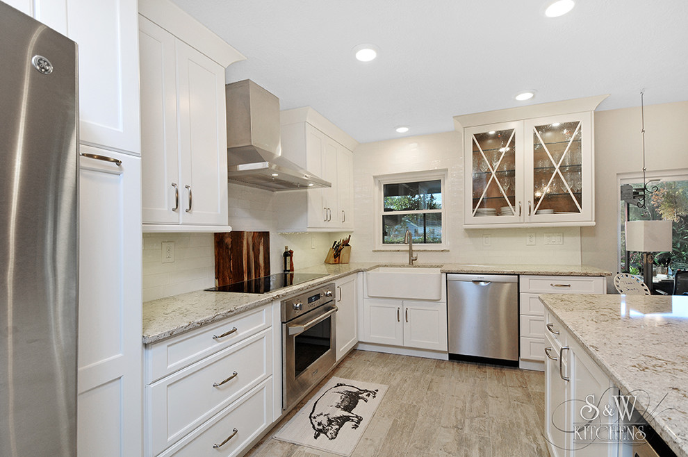 Example of a mid-sized transitional galley porcelain tile eat-in kitchen design in Tampa with a farmhouse sink, flat-panel cabinets, white cabinets, quartz countertops, white backsplash, subway tile backsplash, stainless steel appliances and a peninsula