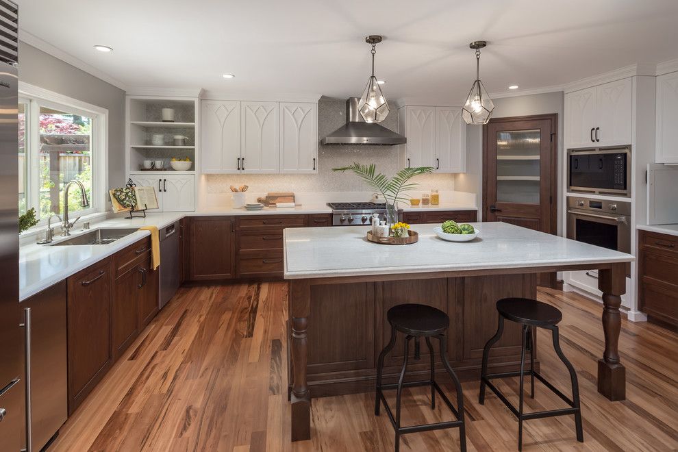 Large traditional u-shaped kitchen in San Francisco with a submerged sink, dark wood cabinets, composite countertops, grey splashback, mosaic tiled splashback, stainless steel appliances, an island, white worktops, recessed-panel cabinets, medium hardwood flooring and brown floors.