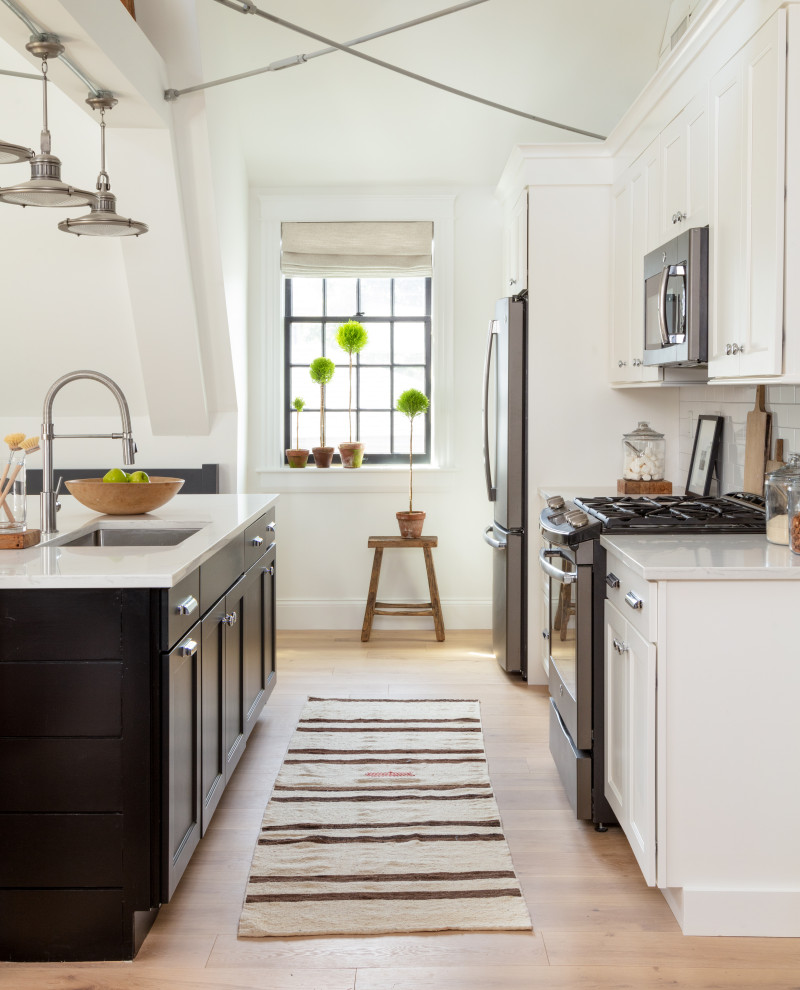 This is an example of a classic cream and black galley kitchen in Boston with a submerged sink, shaker cabinets, white cabinets, stainless steel appliances, medium hardwood flooring, an island, brown floors and white worktops.