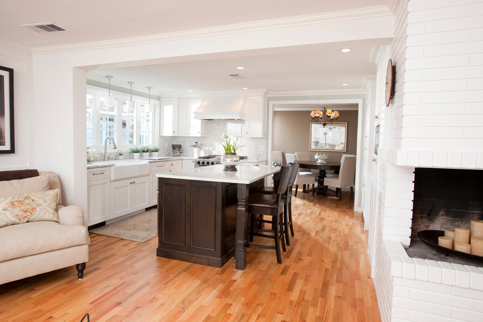 Inspiration for a mid-sized contemporary l-shaped light wood floor and brown floor open concept kitchen remodel in Other with a farmhouse sink, recessed-panel cabinets, white cabinets, white backsplash, stainless steel appliances, marble countertops, stone tile backsplash and an island