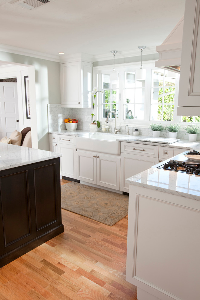 Inspiration for a mid-sized contemporary l-shaped light wood floor and brown floor open concept kitchen remodel in Other with a farmhouse sink, recessed-panel cabinets, white cabinets, marble countertops, white backsplash, stone tile backsplash, stainless steel appliances and an island