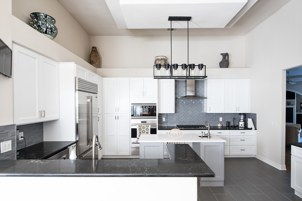 Traditional u-shaped enclosed kitchen in Austin with shaker cabinets, white cabinets, grey splashback, stainless steel appliances, an island and grey floors.