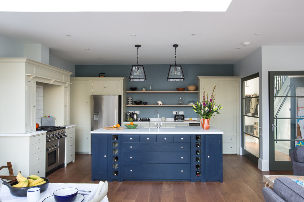 This is an example of a large traditional open plan kitchen in London with a double-bowl sink, blue cabinets, quartz worktops, white splashback, stone slab splashback, stainless steel appliances, dark hardwood flooring and brown floors.