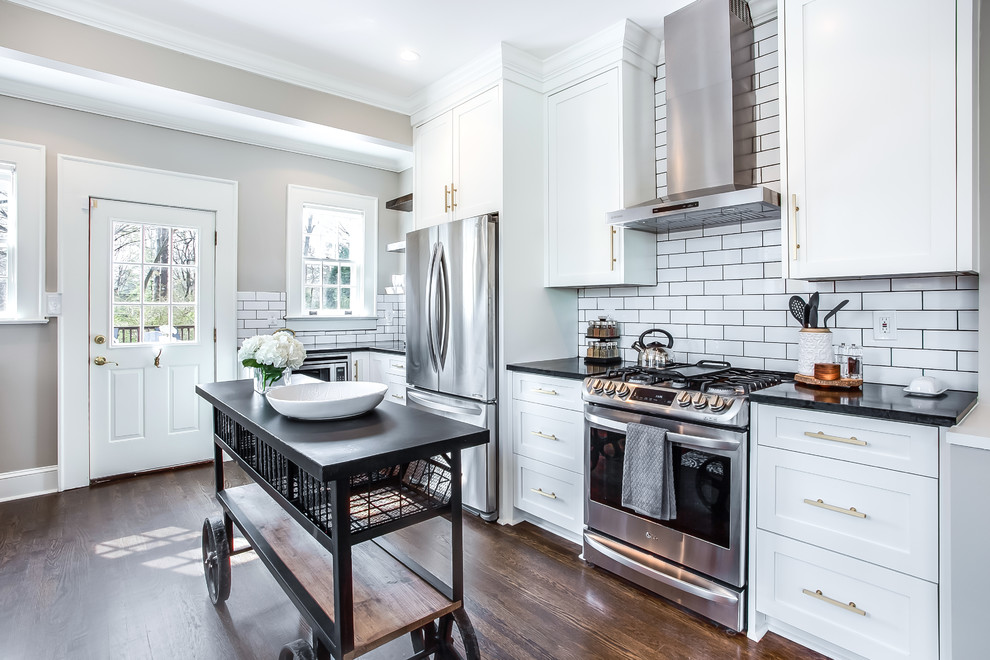 Inspiration for a transitional dark wood floor and brown floor kitchen remodel in Atlanta with shaker cabinets, white cabinets, white backsplash, subway tile backsplash, stainless steel appliances, an island and black countertops