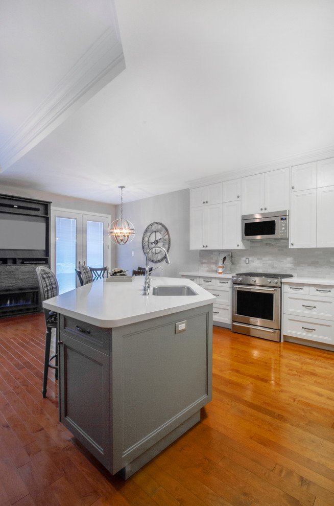 Photo of a medium sized classic l-shaped kitchen in Toronto with a double-bowl sink, recessed-panel cabinets, white cabinets, engineered stone countertops, grey splashback, metro tiled splashback, stainless steel appliances, medium hardwood flooring and an island.