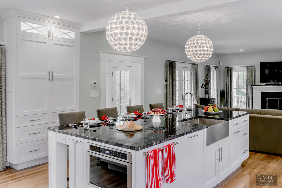 Example of a mid-sized transitional galley light wood floor and beige floor eat-in kitchen design in Boston with a farmhouse sink, shaker cabinets, white cabinets, quartzite countertops, white backsplash, glass tile backsplash, stainless steel appliances and an island