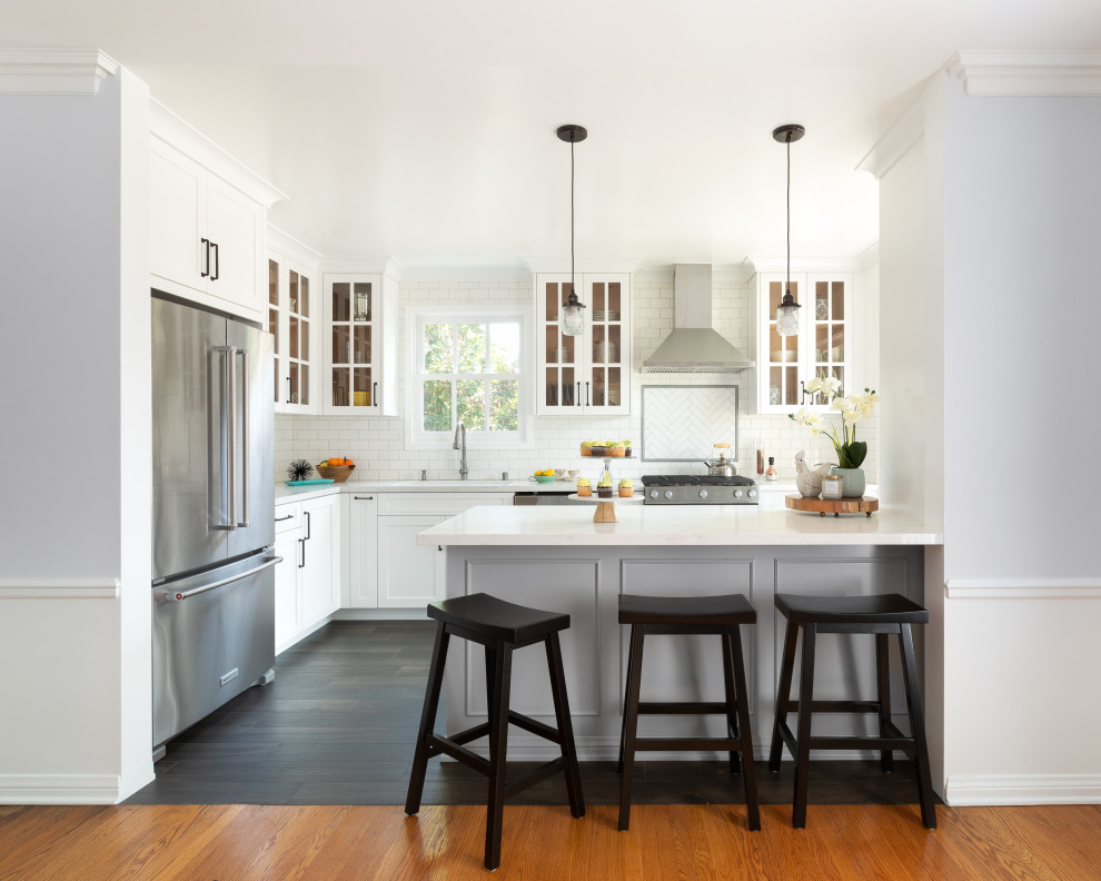 Transitional l-shaped dark wood floor and brown floor kitchen photo in Los Angeles with an undermount sink, shaker cabinets, white cabinets, white backsplash, subway tile backsplash, stainless steel appliances, a peninsula and white countertops
