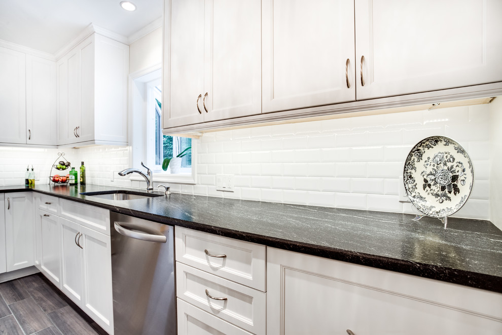 Inredning av ett klassiskt stort u-kök, med en undermonterad diskho, luckor med infälld panel, vita skåp, granitbänkskiva, vitt stänkskydd, stänkskydd i tunnelbanekakel, rostfria vitvaror och en köksö