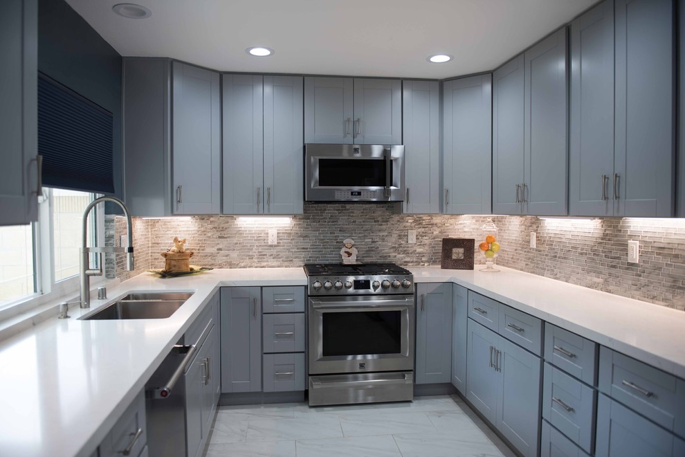 This is an example of a medium sized classic u-shaped enclosed kitchen in Los Angeles with shaker cabinets, engineered stone countertops, no island, a double-bowl sink, blue cabinets, beige splashback, glass tiled splashback, stainless steel appliances and limestone flooring.