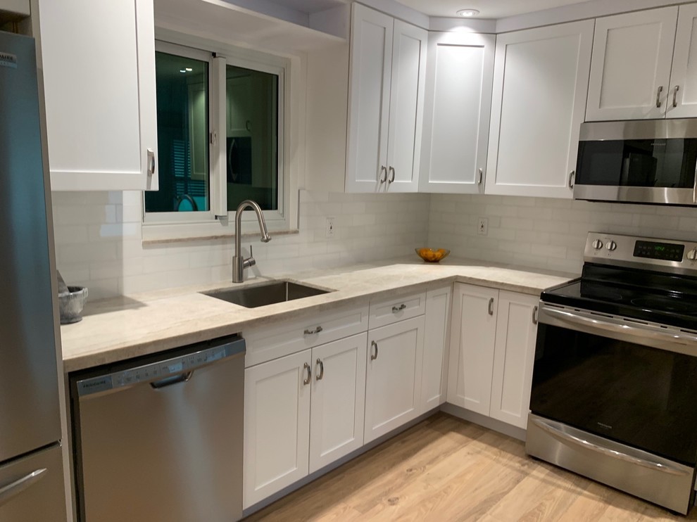 Kitchen - mid-sized transitional l-shaped light wood floor kitchen idea in Miami with an undermount sink, shaker cabinets, white cabinets, limestone countertops, white backsplash, subway tile backsplash, stainless steel appliances, no island and beige countertops