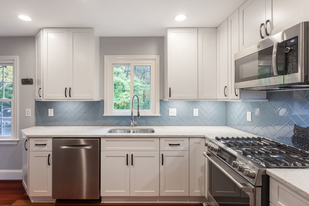 Example of a mid-sized transitional galley medium tone wood floor and brown floor open concept kitchen design in DC Metro with a double-bowl sink, shaker cabinets, white cabinets, quartz countertops, blue backsplash, glass tile backsplash, stainless steel appliances, an island and white countertops