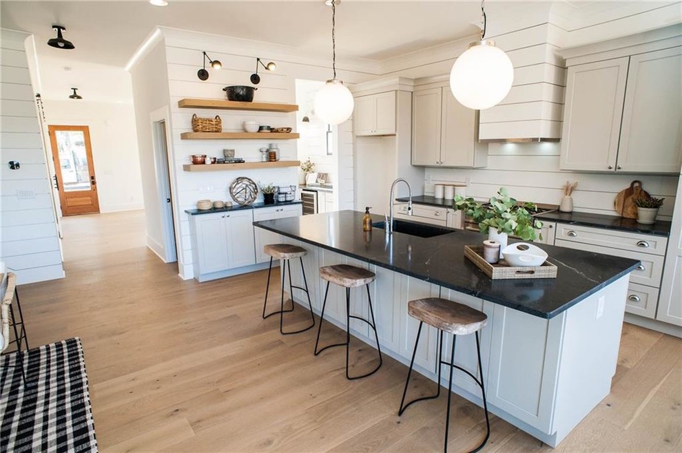 Design ideas for a medium sized classic l-shaped open plan kitchen in Miami with a submerged sink, shaker cabinets, white cabinets, onyx worktops, white splashback, wood splashback, stainless steel appliances, light hardwood flooring, an island, beige floors and black worktops.