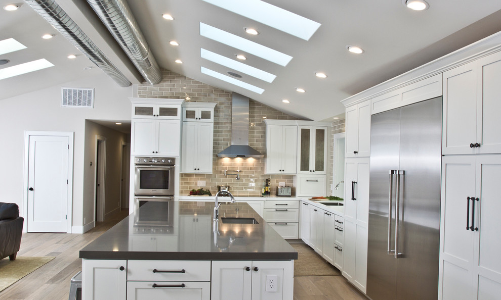 Inspiration for a huge transitional l-shaped light wood floor open concept kitchen remodel in San Francisco with an undermount sink, shaker cabinets, white cabinets, granite countertops, beige backsplash, ceramic backsplash, stainless steel appliances and an island