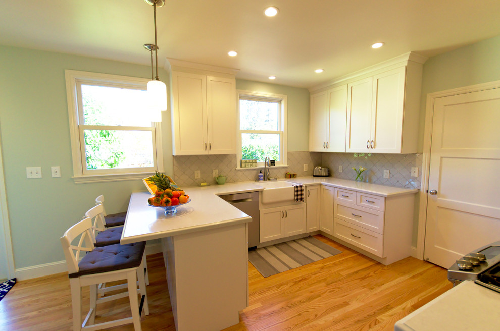 Small transitional u-shaped laminate floor and beige floor enclosed kitchen photo in San Francisco with a farmhouse sink, shaker cabinets, white cabinets, stainless steel appliances, a peninsula, solid surface countertops and window backsplash
