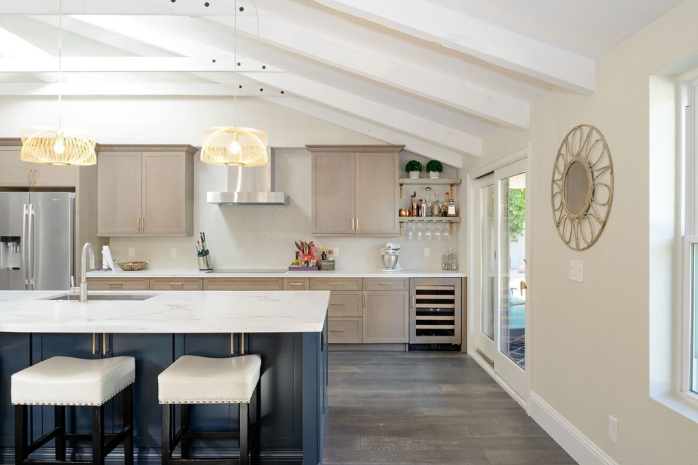 Inredning av ett modernt stort vit vitt kök, med en undermonterad diskho, skåp i shakerstil, blå skåp, bänkskiva i kvarts, vitt stänkskydd, stänkskydd i porslinskakel, rostfria vitvaror, mellanmörkt trägolv, en köksö och flerfärgat golv