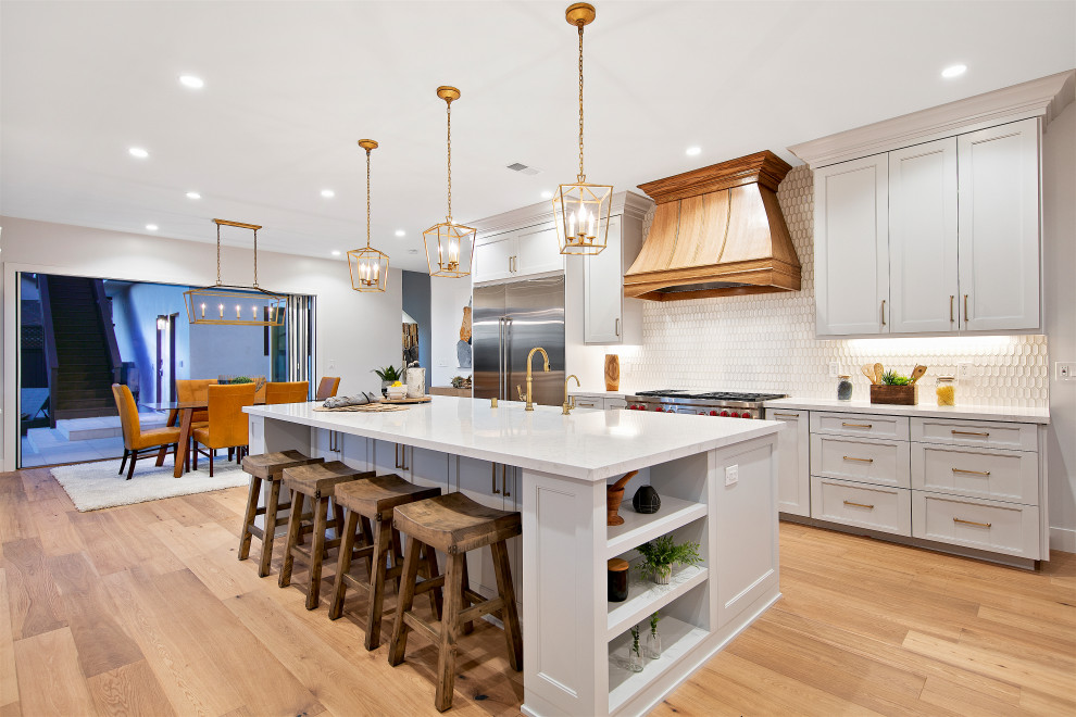 Transitional galley medium tone wood floor and brown floor kitchen photo in San Diego with a farmhouse sink, shaker cabinets, white cabinets, white backsplash, mosaic tile backsplash, stainless steel appliances, an island and white countertops