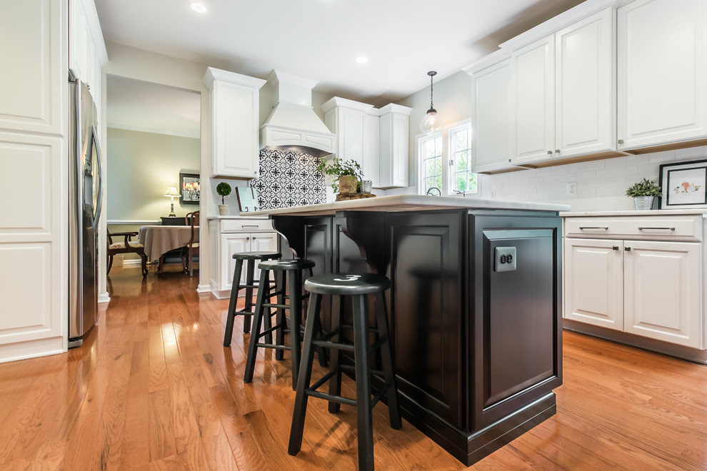 Example of a large transitional l-shaped medium tone wood floor eat-in kitchen design in DC Metro with an undermount sink, raised-panel cabinets, white cabinets, quartz countertops, white backsplash, cement tile backsplash, stainless steel appliances and an island