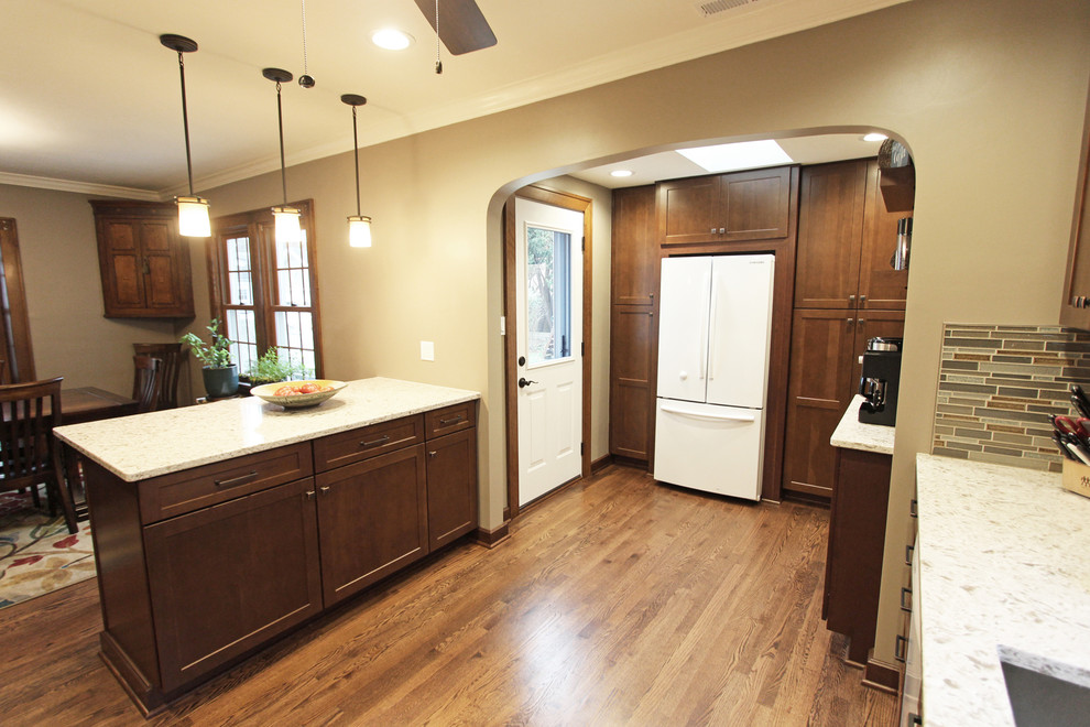 Inredning av ett klassiskt mellanstort kök, med en undermonterad diskho, skåp i shakerstil, skåp i mellenmörkt trä, bänkskiva i kvarts, brunt stänkskydd, stänkskydd i glaskakel, vita vitvaror, mellanmörkt trägolv, en köksö och brunt golv