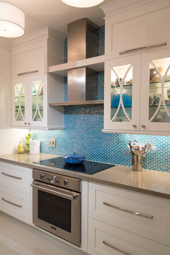 Small trendy galley kitchen photo in Philadelphia with glass-front cabinets, white cabinets, quartz countertops, blue backsplash, glass tile backsplash and stainless steel appliances