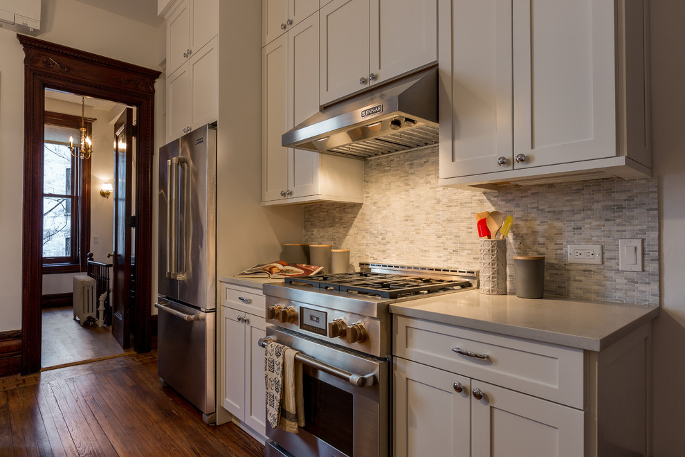 Mid-sized transitional galley medium tone wood floor and brown floor kitchen photo in New York with an undermount sink, shaker cabinets, white cabinets, quartzite countertops, beige backsplash, matchstick tile backsplash, stainless steel appliances and an island