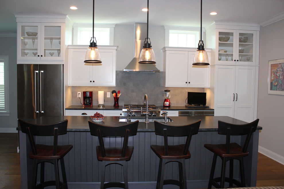 Idéer för mellanstora vintage svart u-kök, med en undermonterad diskho, luckor med infälld panel, vita skåp, granitbänkskiva, grått stänkskydd, stänkskydd i travertin, rostfria vitvaror, mellanmörkt trägolv och en köksö