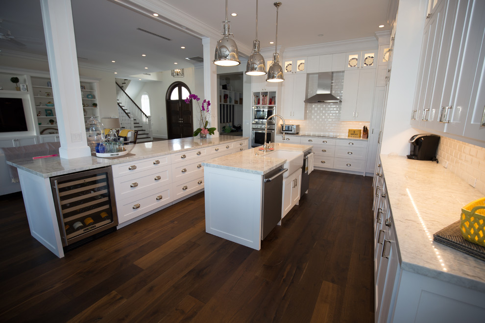 Eat-in kitchen - large transitional u-shaped medium tone wood floor eat-in kitchen idea in Miami with a farmhouse sink, shaker cabinets, white cabinets, granite countertops, white backsplash, subway tile backsplash, paneled appliances and two islands