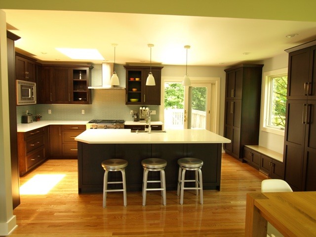 Eat-in kitchen - mid-sized transitional l-shaped light wood floor and beige floor eat-in kitchen idea in New York with shaker cabinets, brown cabinets, quartz countertops, blue backsplash, an island, a farmhouse sink, glass tile backsplash and stainless steel appliances