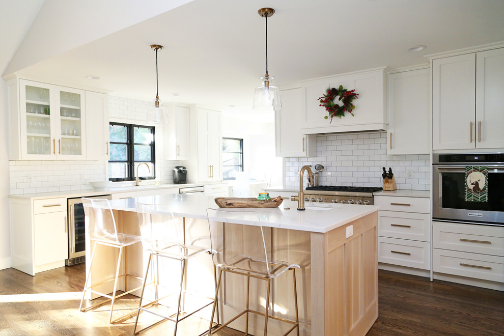 Klassische Küche in U-Form mit Schrankfronten im Shaker-Stil, weißen Schränken, Küchenrückwand in Weiß, Rückwand aus Metrofliesen, Küchengeräten aus Edelstahl, braunem Holzboden und Kücheninsel in Orange County