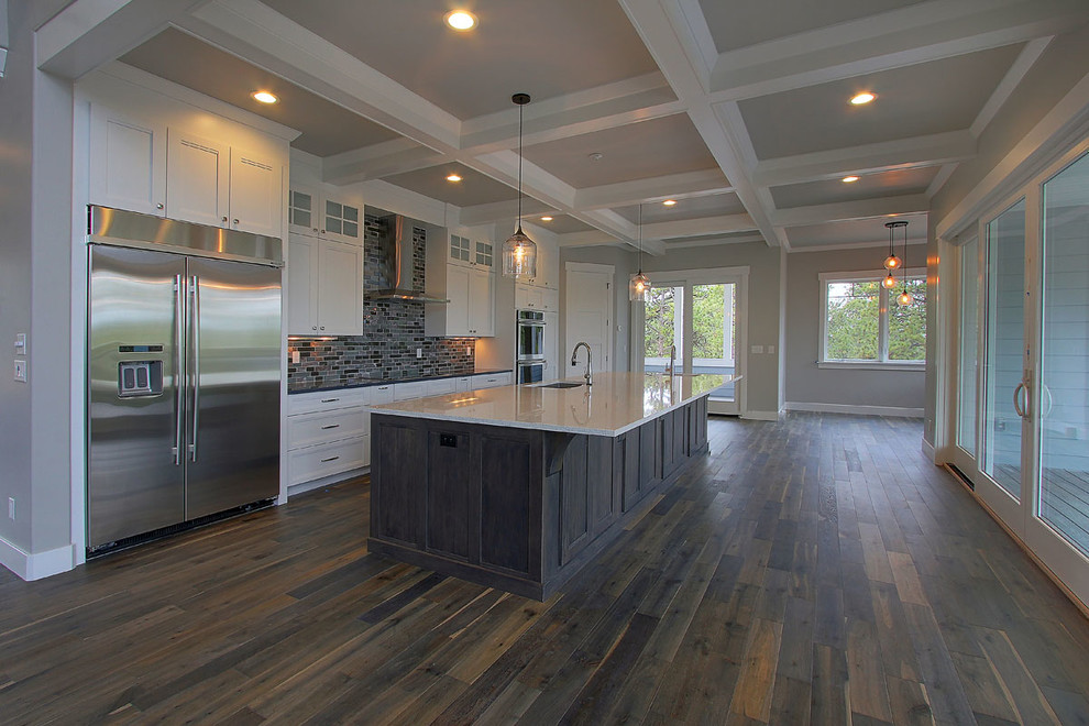 Design ideas for a large traditional galley open plan kitchen in Denver with a submerged sink, recessed-panel cabinets, grey cabinets, engineered stone countertops, grey splashback, glass tiled splashback, stainless steel appliances, dark hardwood flooring and an island.
