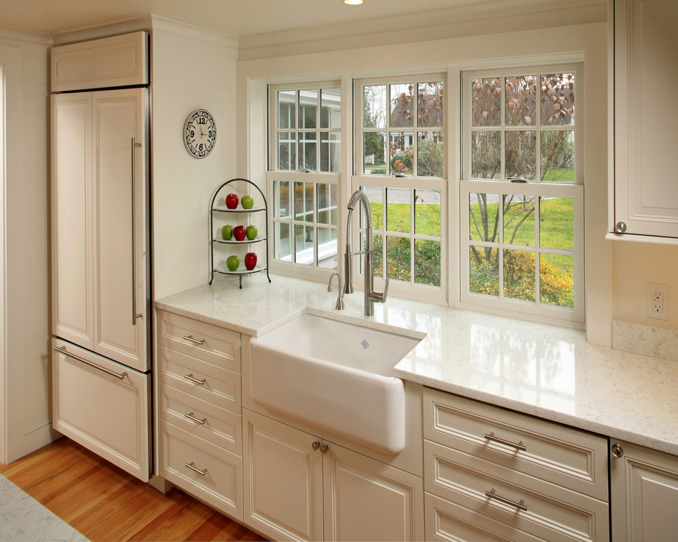 Eat-in kitchen - mid-sized transitional l-shaped medium tone wood floor eat-in kitchen idea in Boston with white cabinets, an island, a farmhouse sink, raised-panel cabinets, marble countertops, white backsplash, glass sheet backsplash and stainless steel appliances